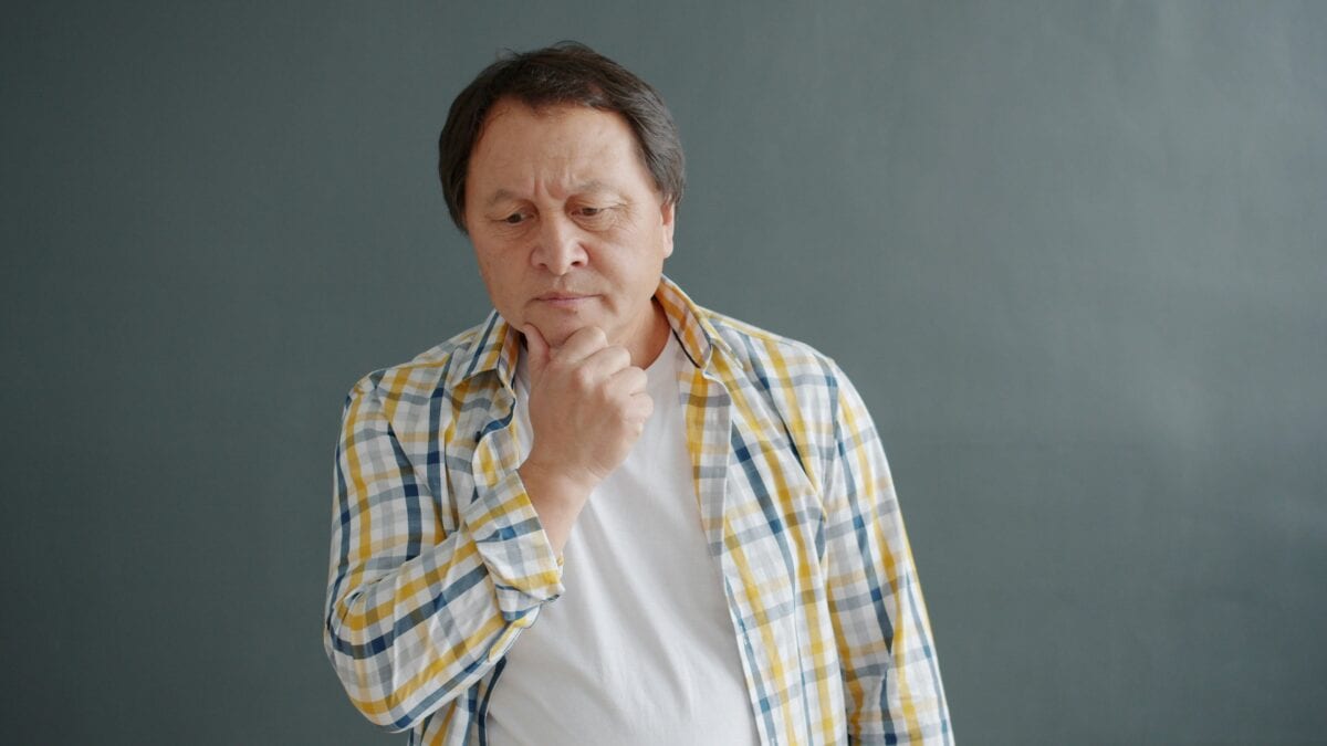 An older man in a blue and yellow checked shirt with his hand on his chin